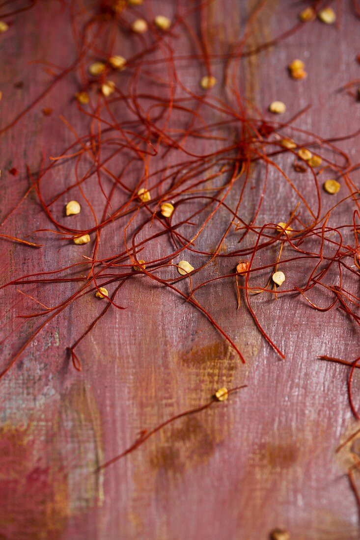 Chilli strands and chilli seeds on a red surface