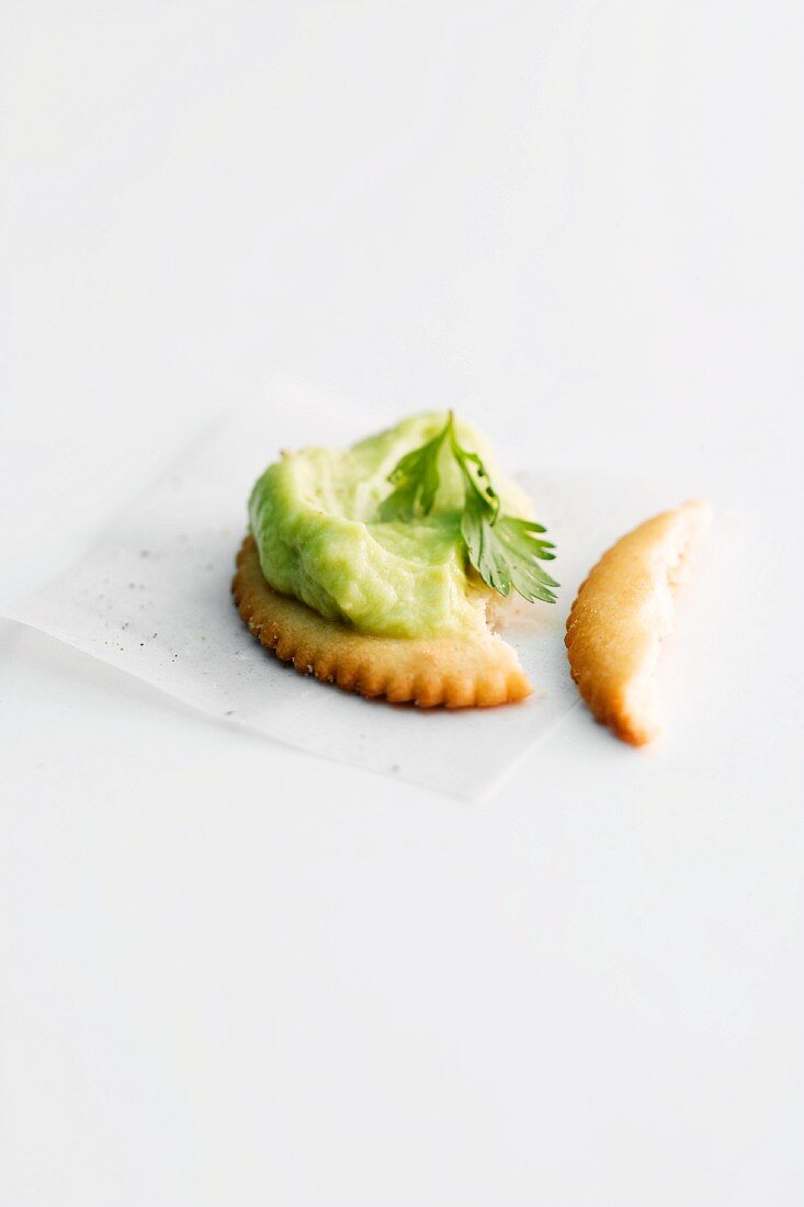 A cracker topped with avocado paste, partly eaten