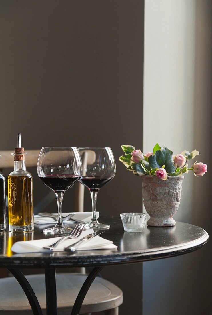 A table laid for a meal in a restaurant, with olive oil, glasses of red wine and a bunch of roses