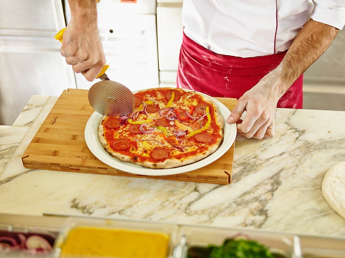 A chef cutting a pizza into portions using a pizza wheel