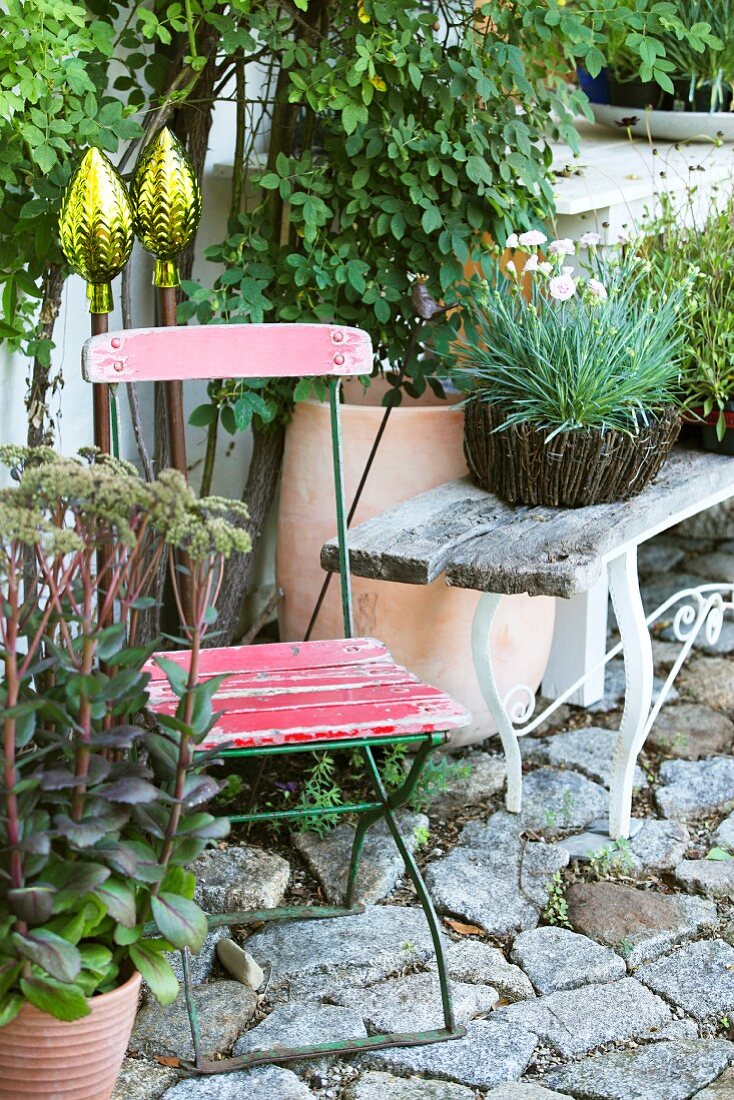 Decorative rods, old garden furniture and potted plants on stone cobbles in garden