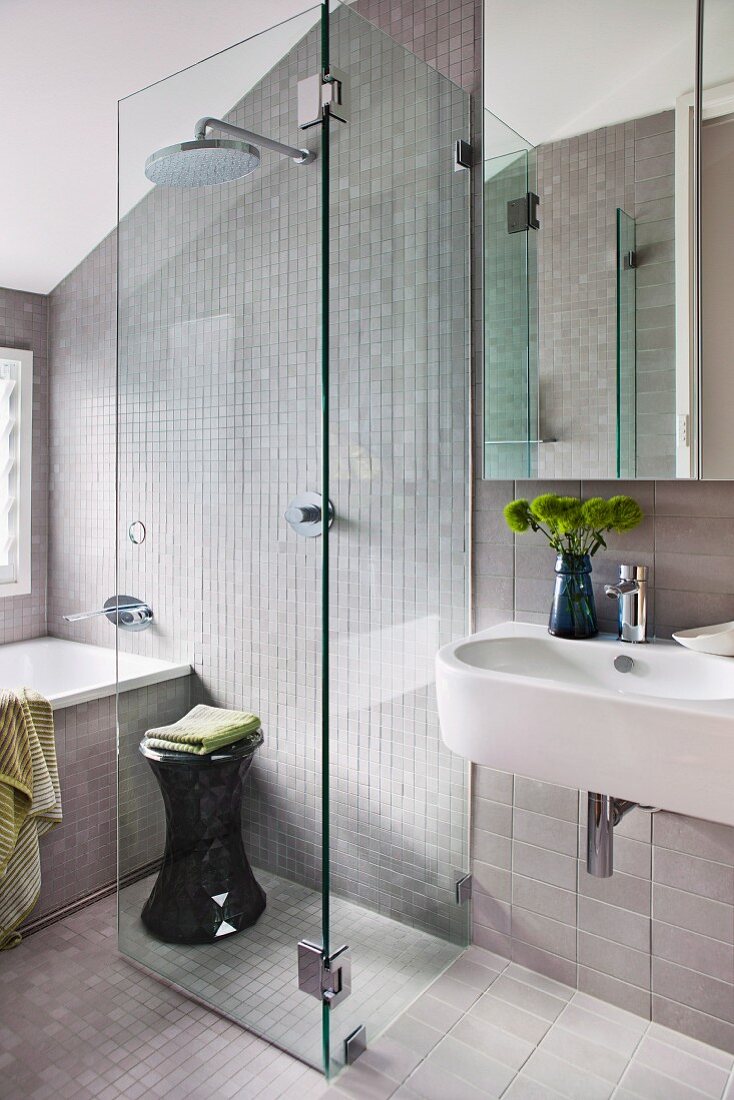 Mosaic tiles in area of bathtub and floor-level rainfall shower with clear glass screen; strip tiles around sink