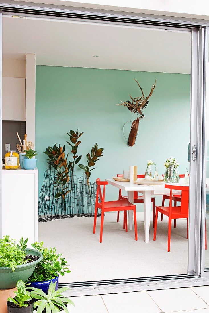View through open sliding, balcony door to red chairs around white table in front of pastel turquoise wall and flower arrangements