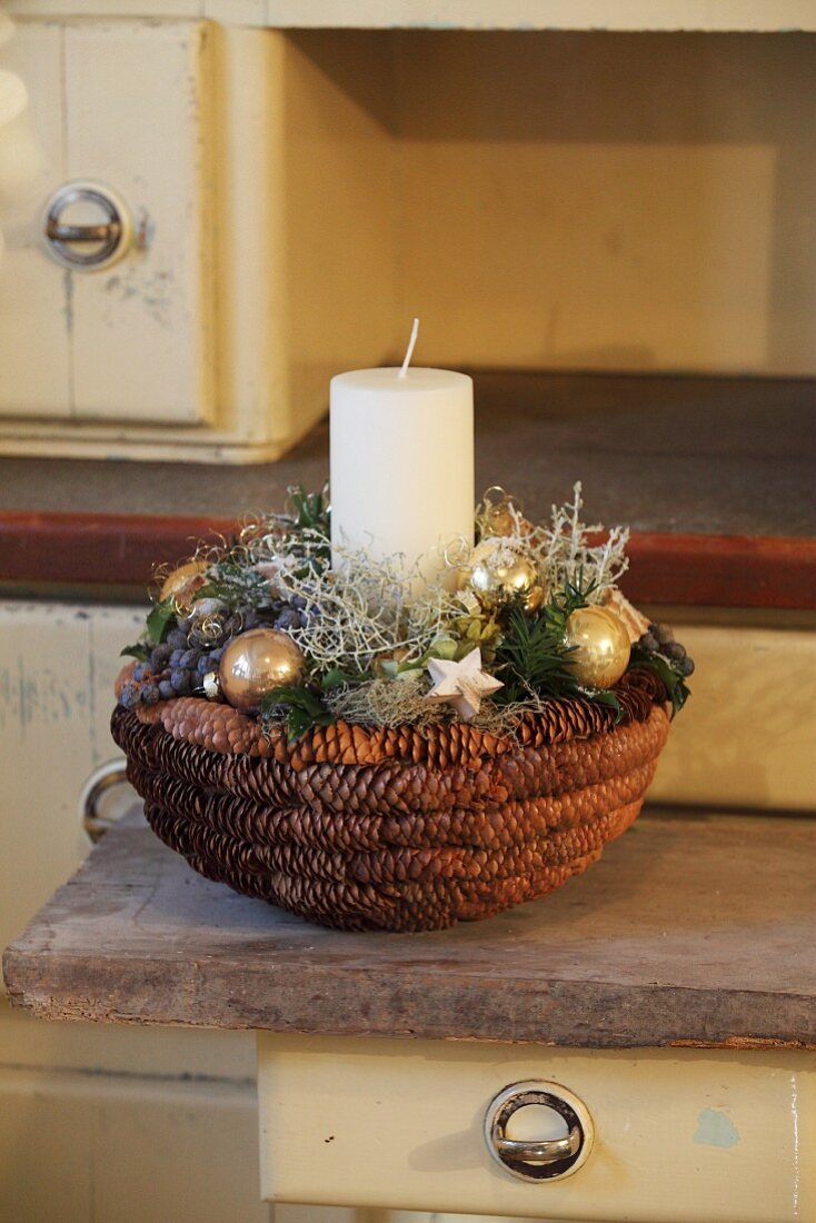 Festive arrangement with candle in basket made from pine cones