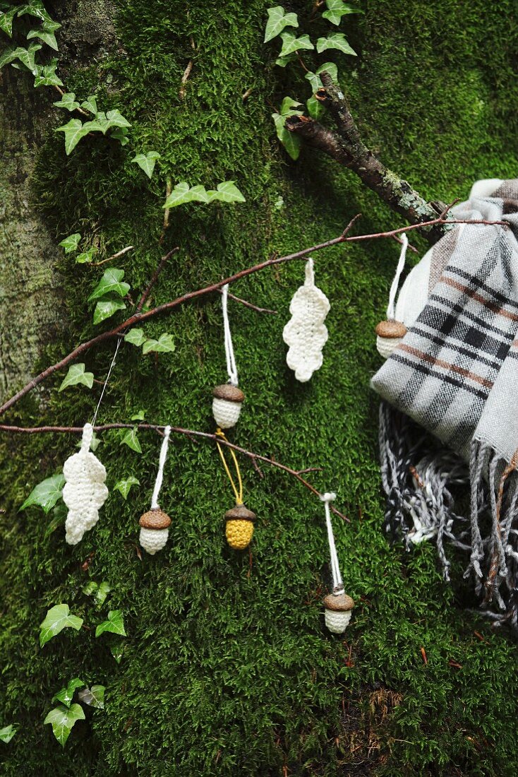 Crocheted acorns and leaves hanging from twigs on mossy boulder