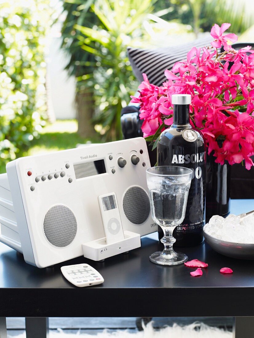 Musikanlage mit iPod neben Schnapsglas und Wodkaflasche vor pinkfarbenem Blumenstrauss auf schwarzem Beistelltisch