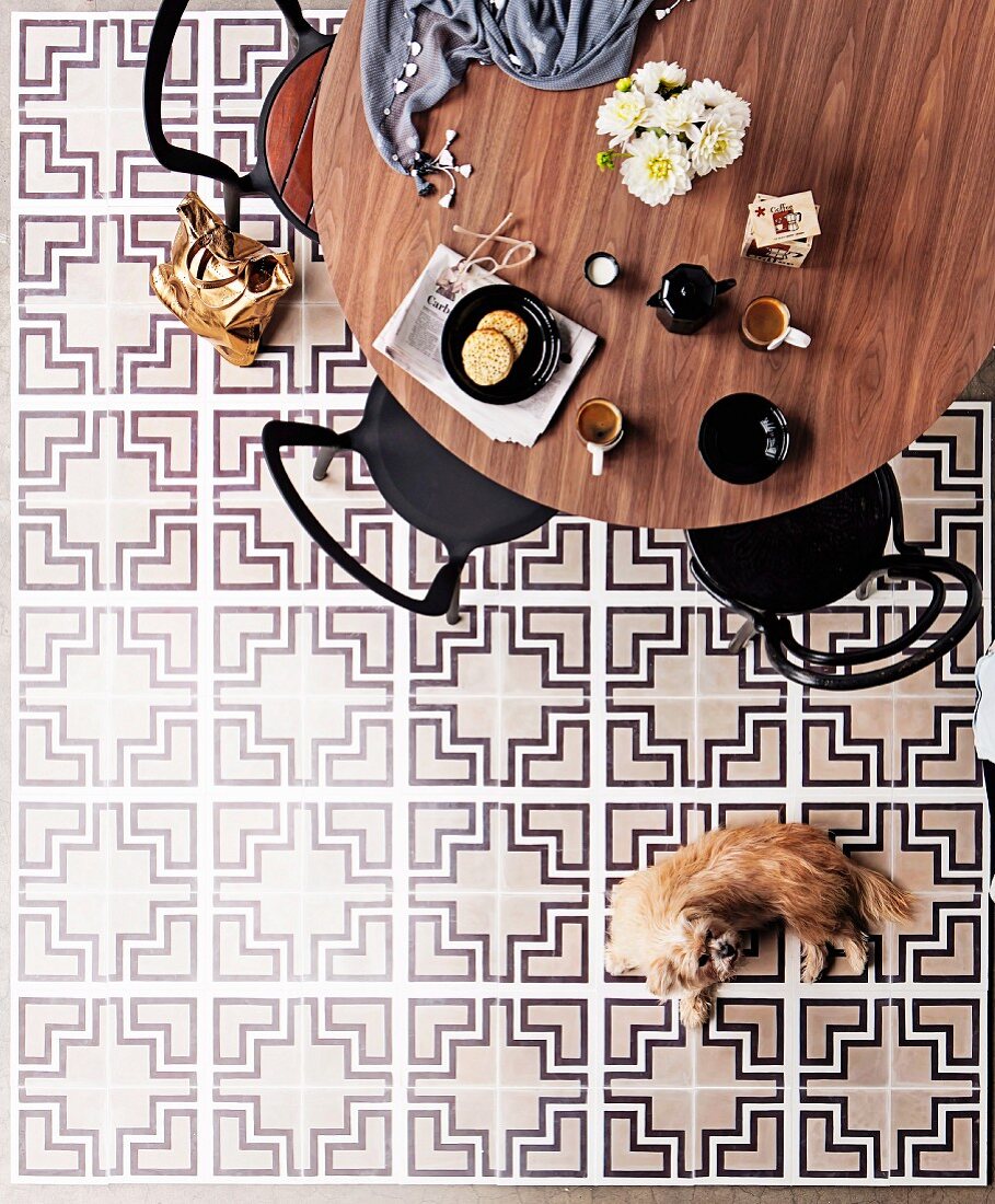 Round dining table and chairs on tiled floor with decorative graphic pattern in black, white & grey