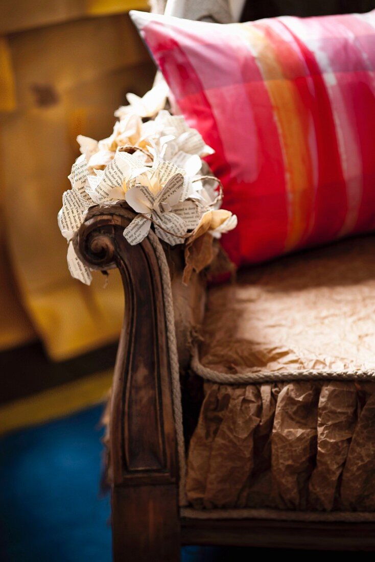 Patterned scatter cushion on armchair with paper flowers decorating armrest