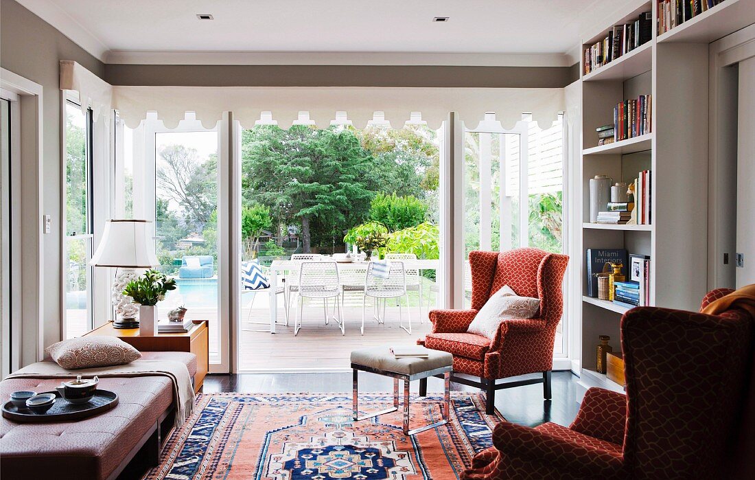 Living area with patterned, wing-back chair and Oriental rug in front of terrace doors