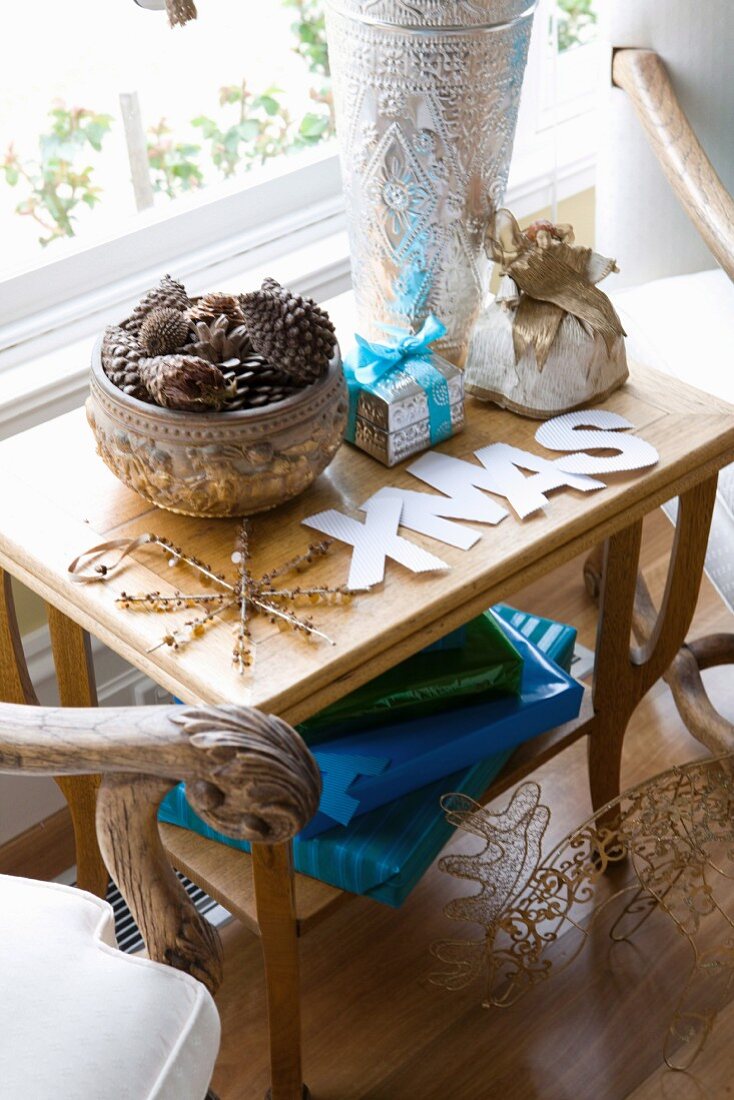 Elegantly wrapped gifts next to a bowl with a cone collection and XMAS letters