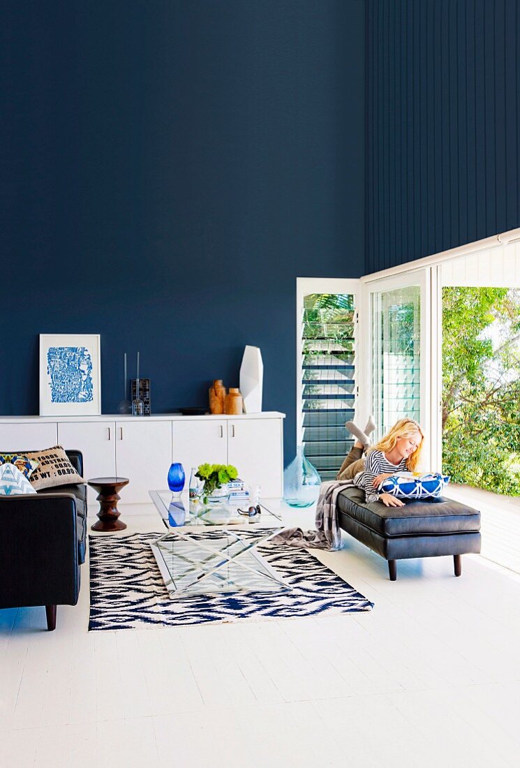 Elegantes Wohnzimmer mit dunkelblauer Wand, lesende Frau vor offener Terrassentür