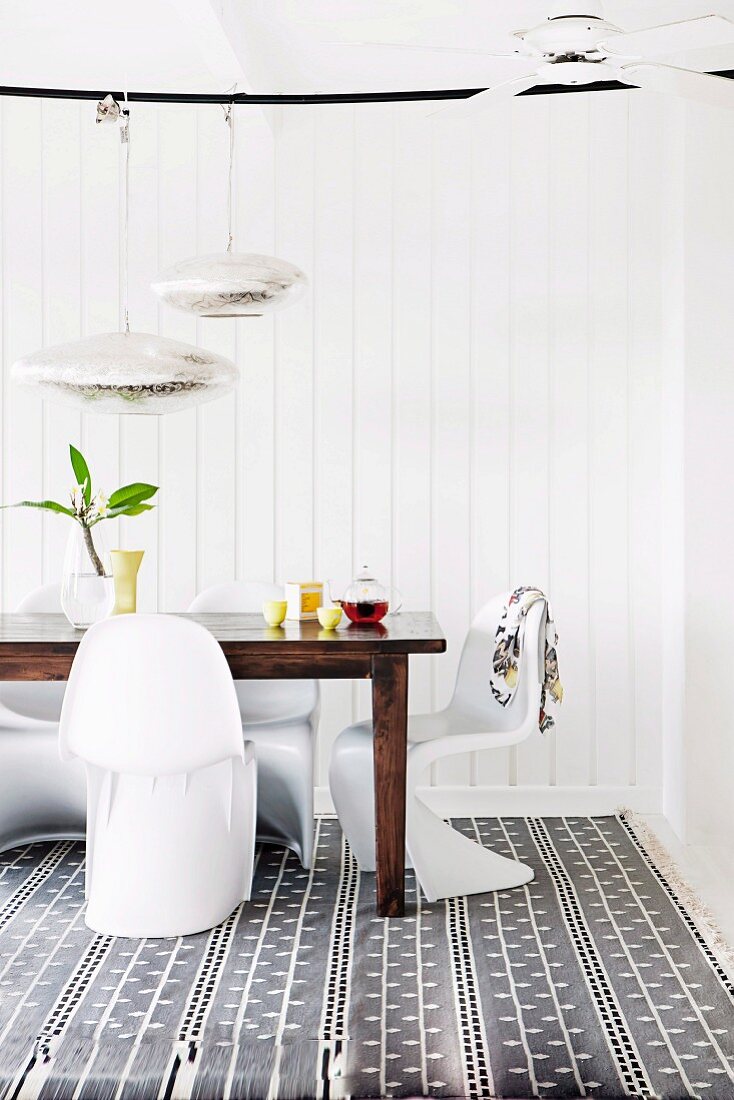 Dining area with white panton chairs and wooden table on patterned carpet in front of white wall covering