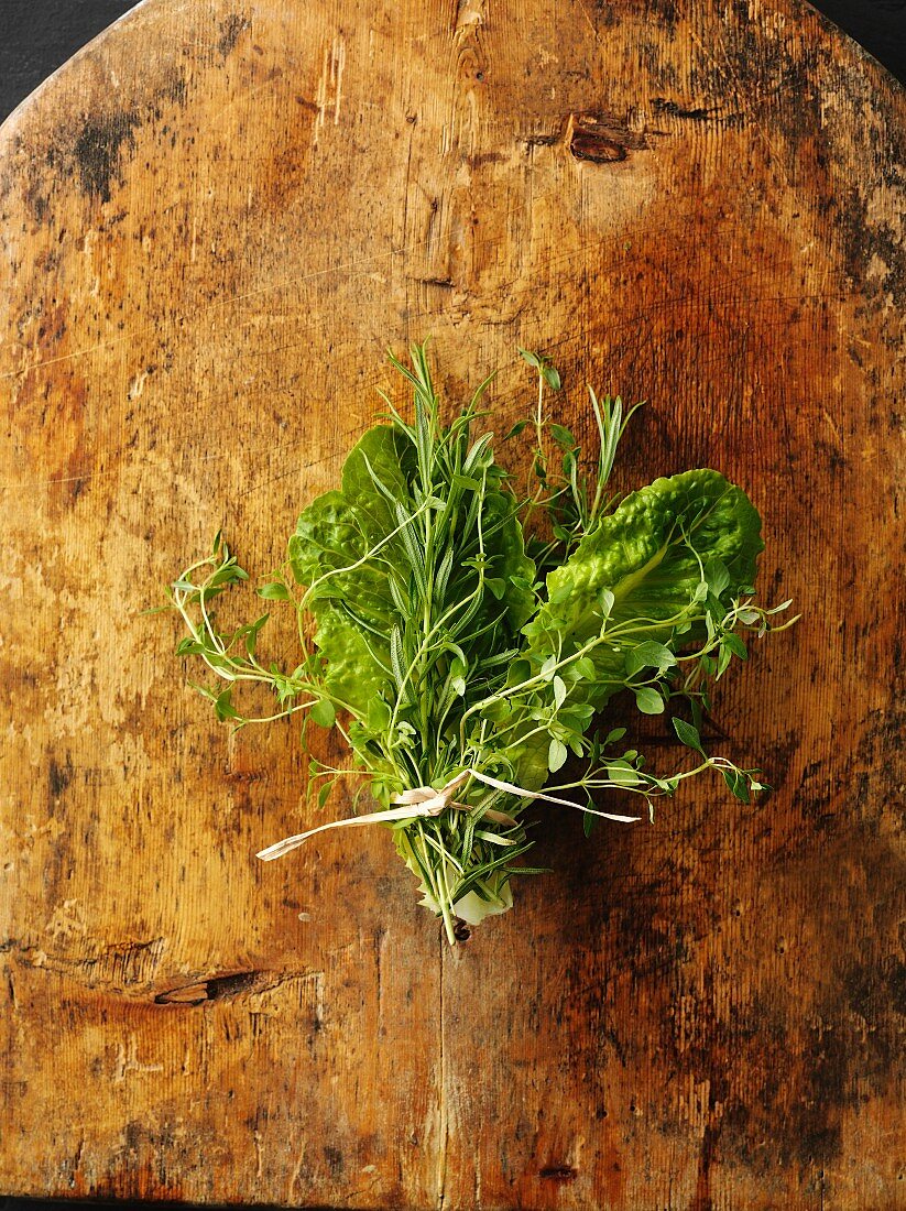 A bunch of herbs with lettuce leaves on a wooden board