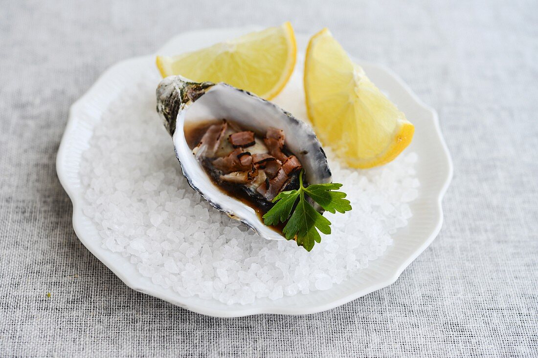 A fresh oyster with lemon wedges on rock salt