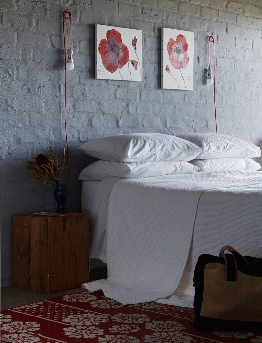 Double bed below red and white floral paintings and innovative sconce lamps on brick wall painted dark grey