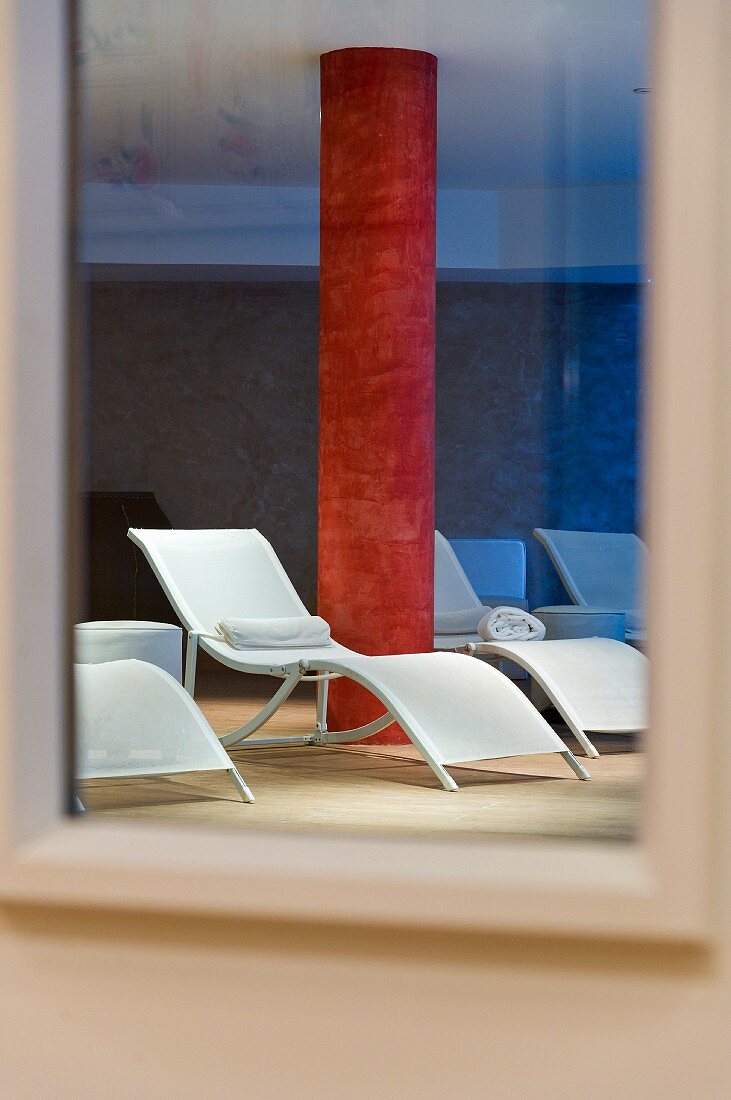 Lounges and red marbled concrete column in a spa's relaxation area reflected in a mirror