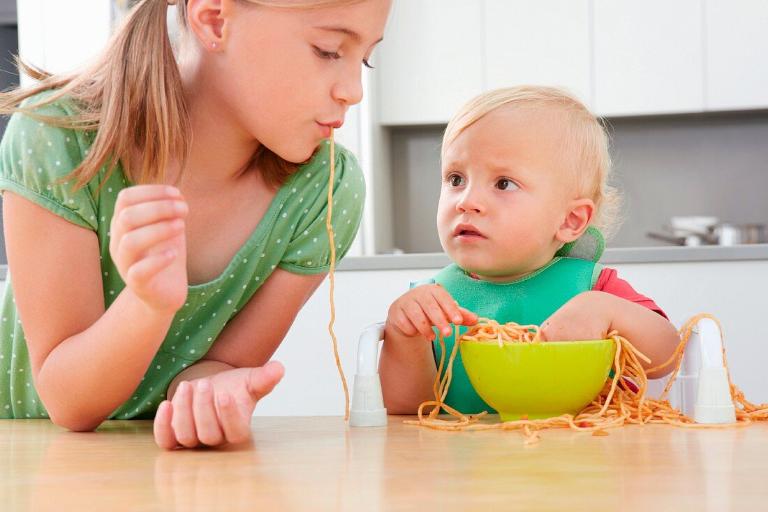 A girl and a small child playing with spaghetti