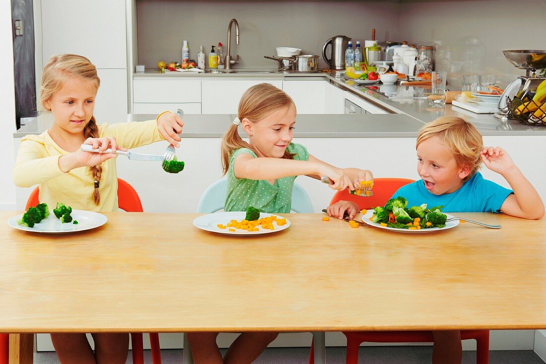 Drei Kinder spielen mit Gemüse am Tisch in der Küche