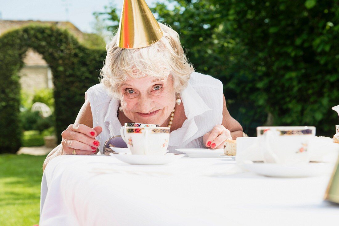 An older woman wearing a party hat sitting at a table in the garden