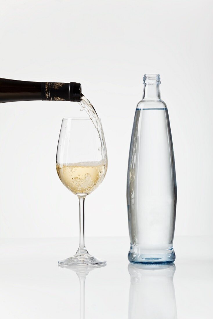 White wine being poured into a glass, next to a bottle of water