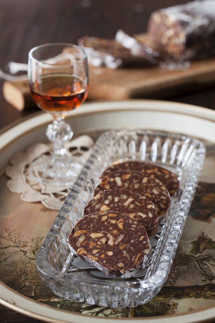 Schokoladen-Biskuit-Salami mit Walnüssen und Rum auf Kristallplatte mit Weinbrand