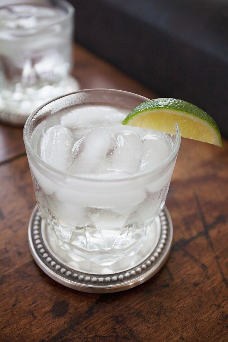 A glass of gin and tonic with ice cubes and a slice of lime