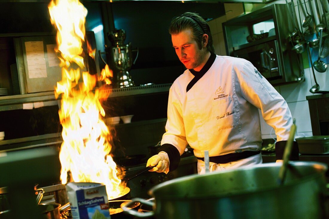 A chef with a flaming pan in a restaurant kitchen