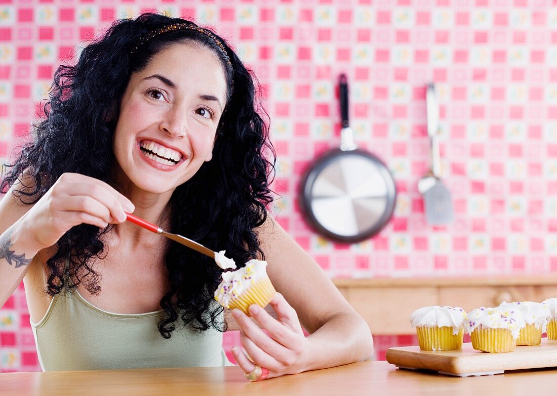 Junge Frau streicht Zuckerguss auf Cupcakes