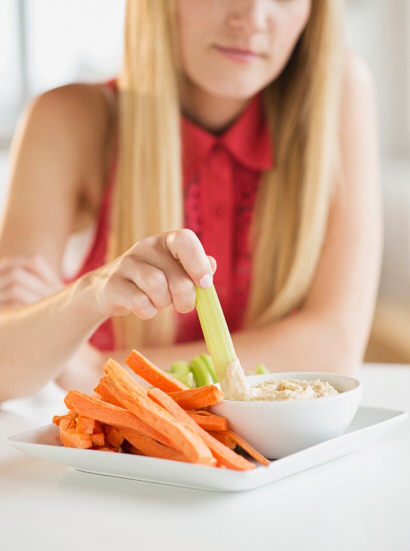 A woman eating raw vegetables with dip