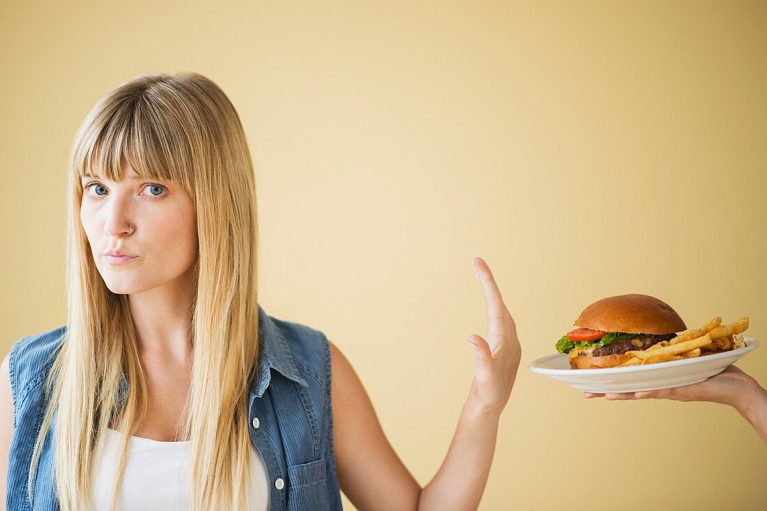 A woman declining a plate of hamburger and chips