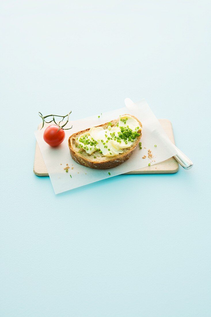 Bread and butter with chives and tomato on a wooden board