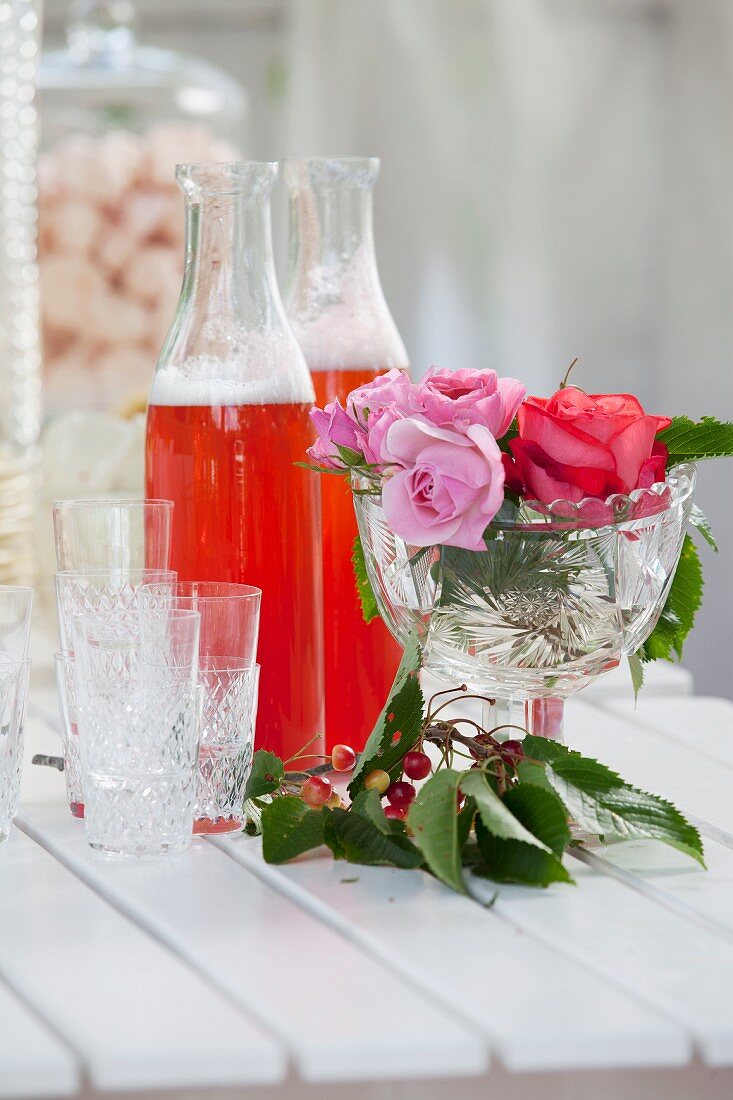 Limonade in Glasflaschen mit Gläsern & Rosendeko auf Tisch