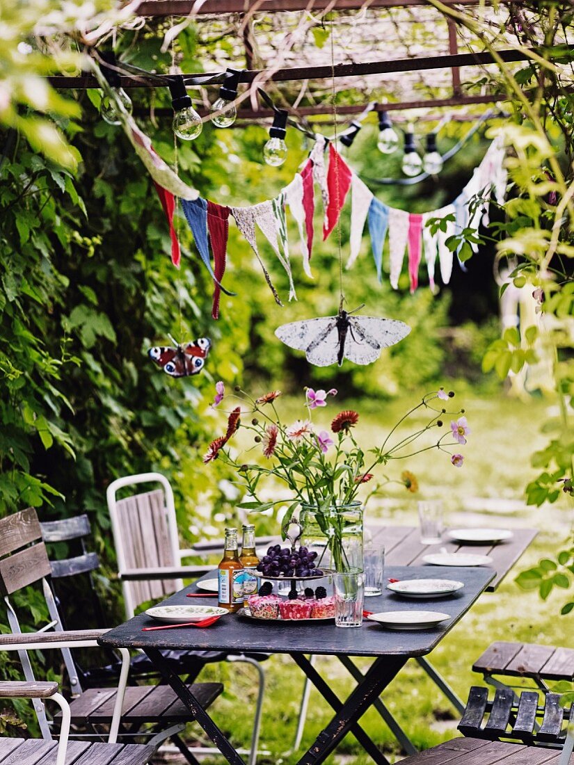 Gedeckter Tisch für Kinderparty im Garten unter Wimpelkette und Glühbirnen
