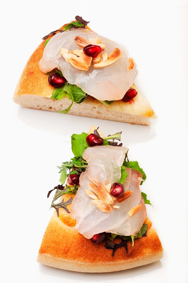 Pizza with fish carpaccio, rocket, almonds and pomegranate seeds