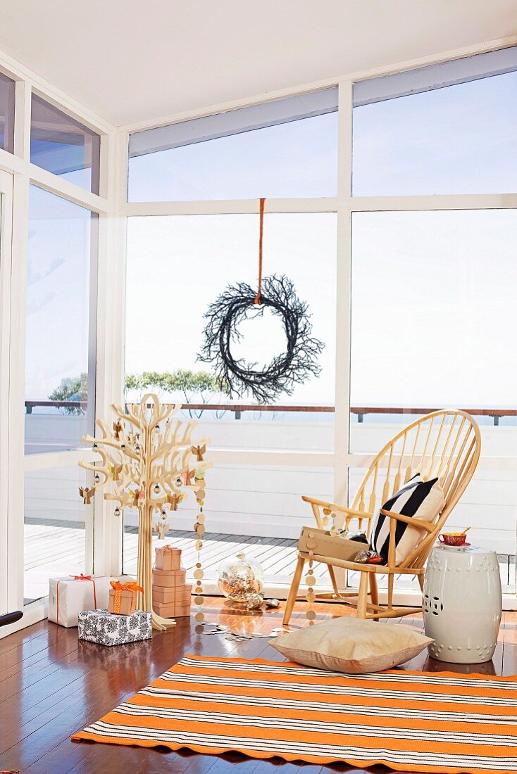 Presents under a stylized Christmas tree and classic chair in front of a window with a decorative wreath