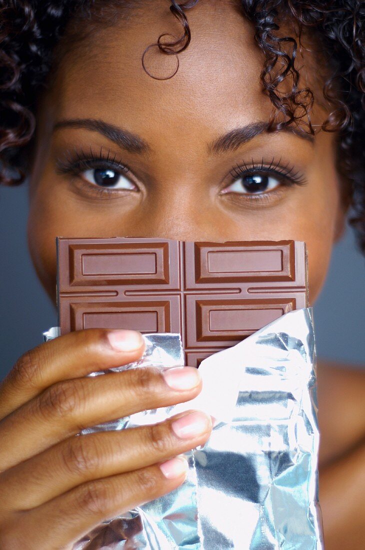 African woman holding chocolate bar in front of face