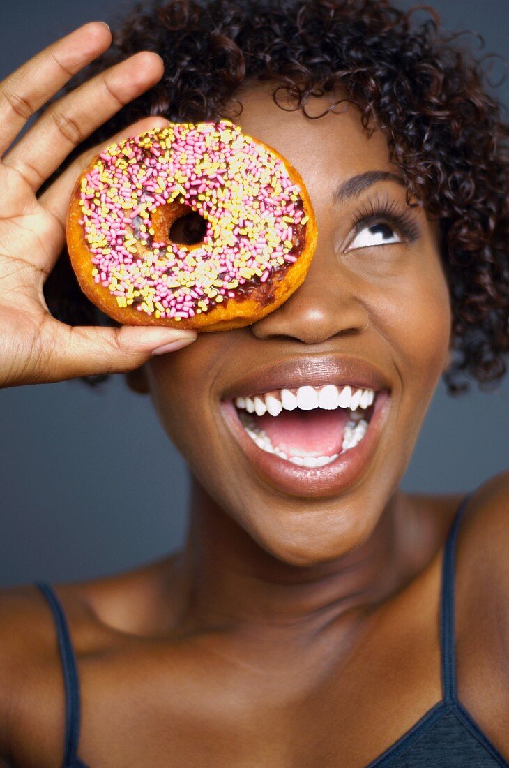 African woman holding doughnut over eye