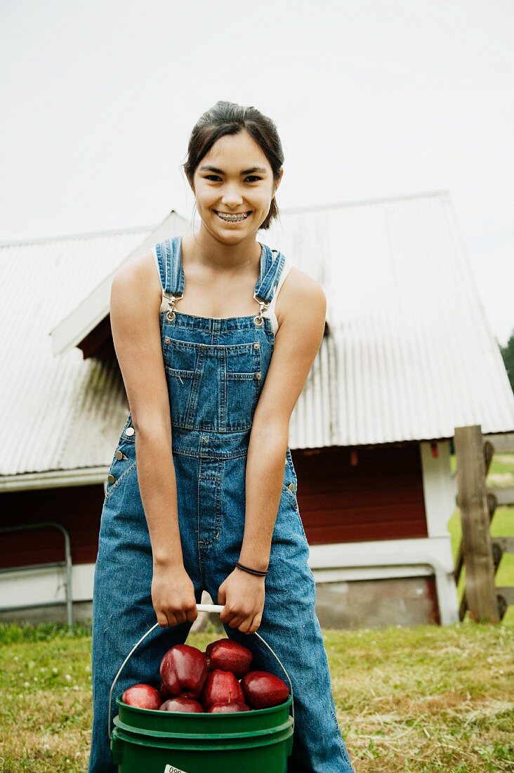 Girl carrying bucket of apples on farm