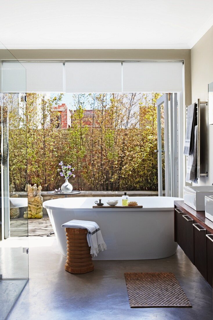 Freistehende Badewanne in modernem Bad vor offener Terrassentür und Blick in Innenhof