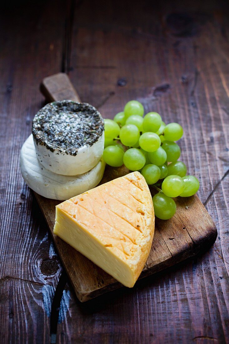 Various types of cheese on a wooden board with green grapes