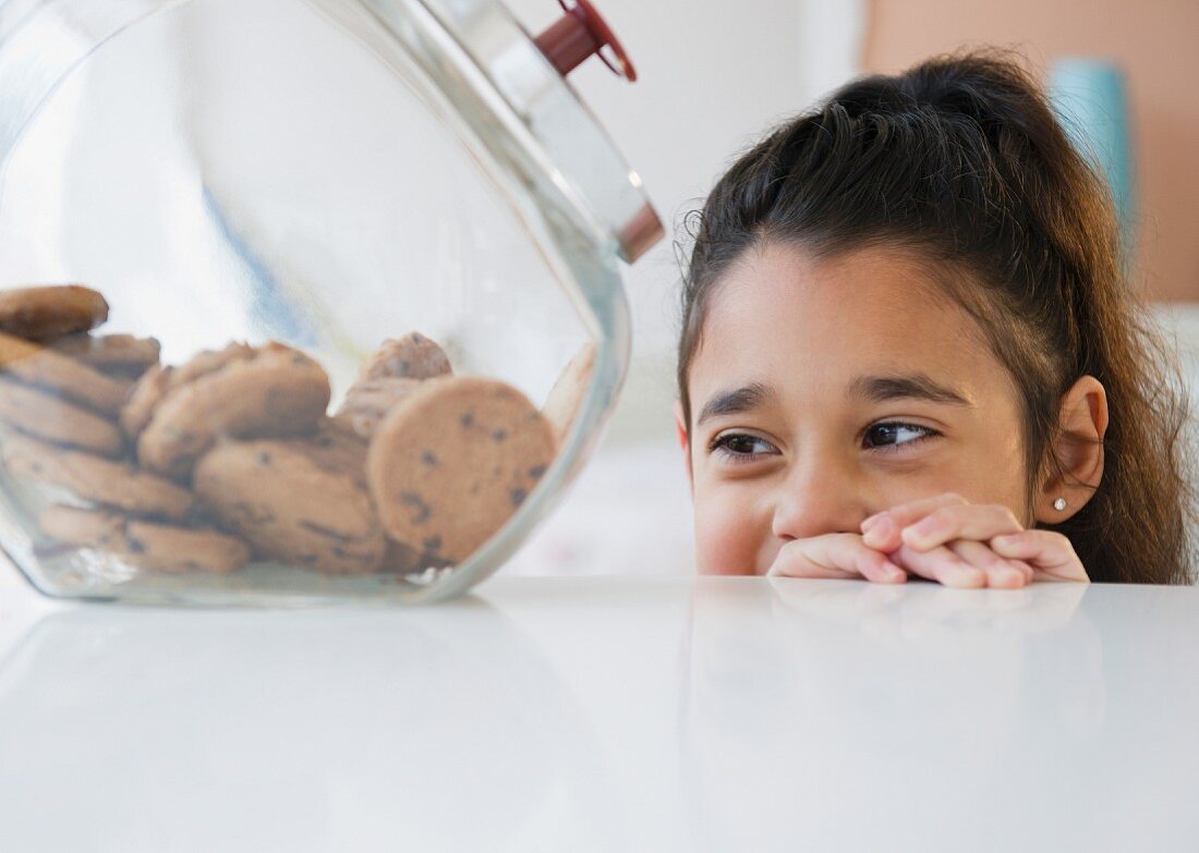 Mixed race girl looking at cookies in cookie jar