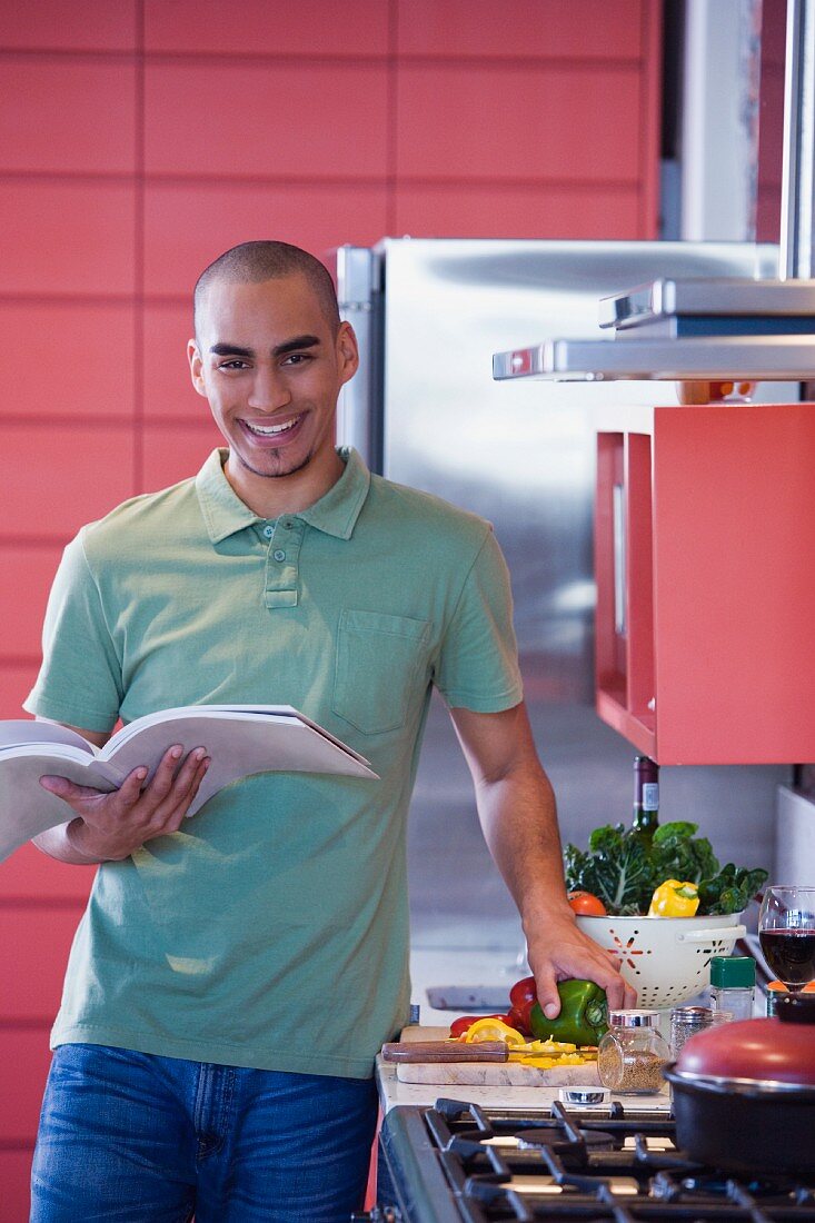 Junger Mann mit Kochbuch beim Kochen