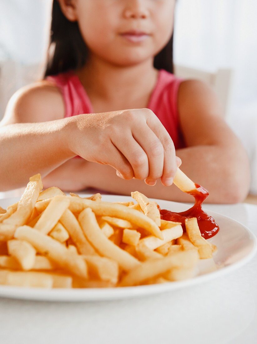 Mädchen isst Pommes Frites mit Ketchup