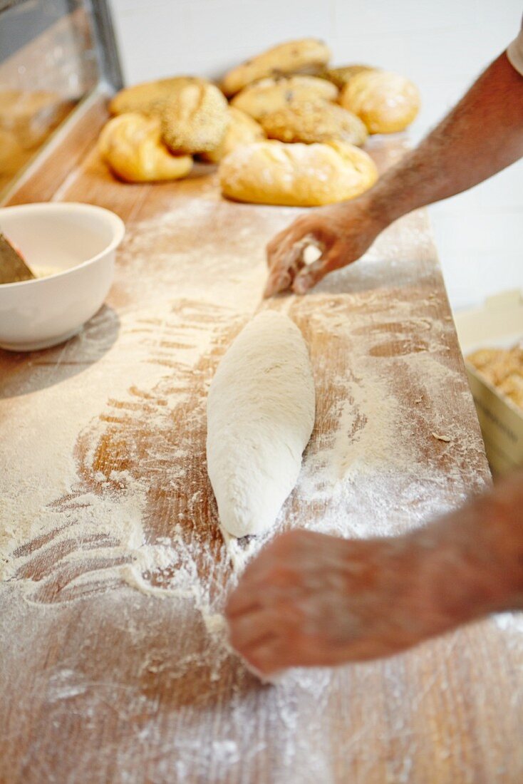 A baker shaping an oblong loaf on a floured wooden board