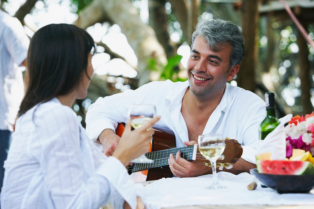 Südamerikanischer Mann spielt Gitarre für Frau beim Gartentisch