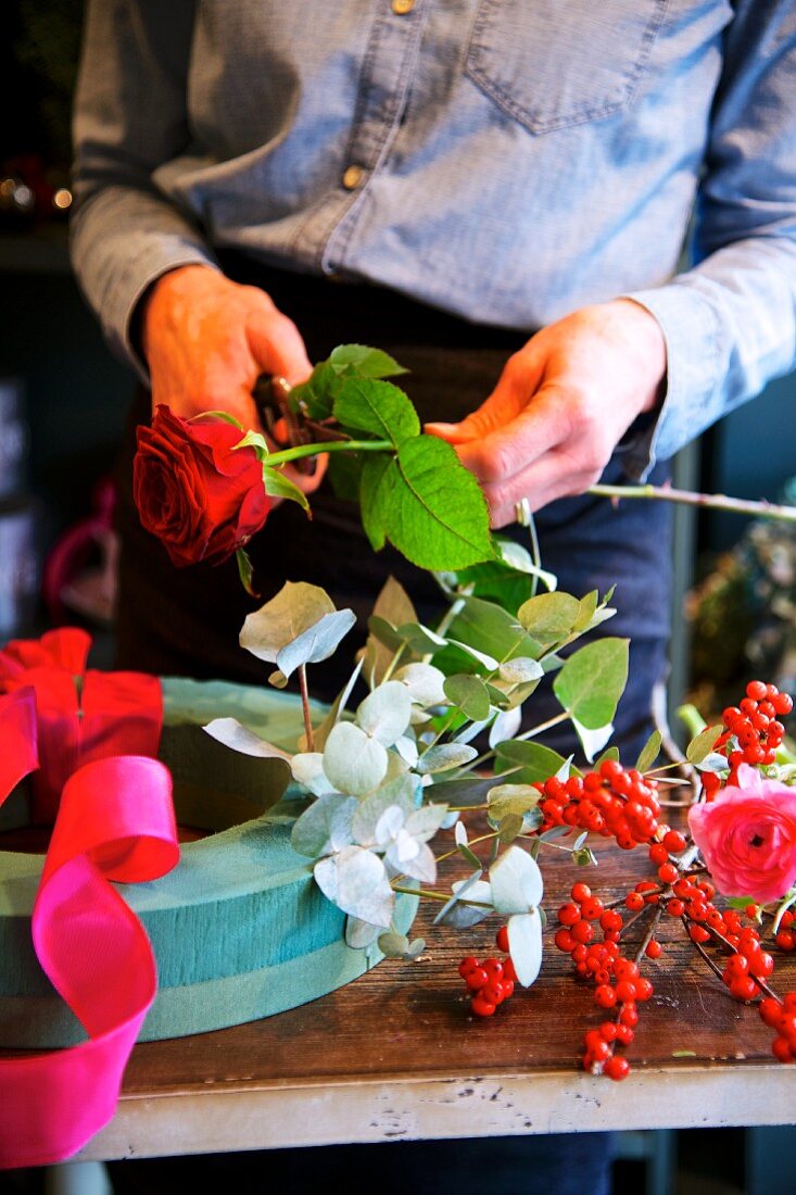 Frauenhände beim Schneiden einer Rose für einen Blumenkranz aus Steckschaum