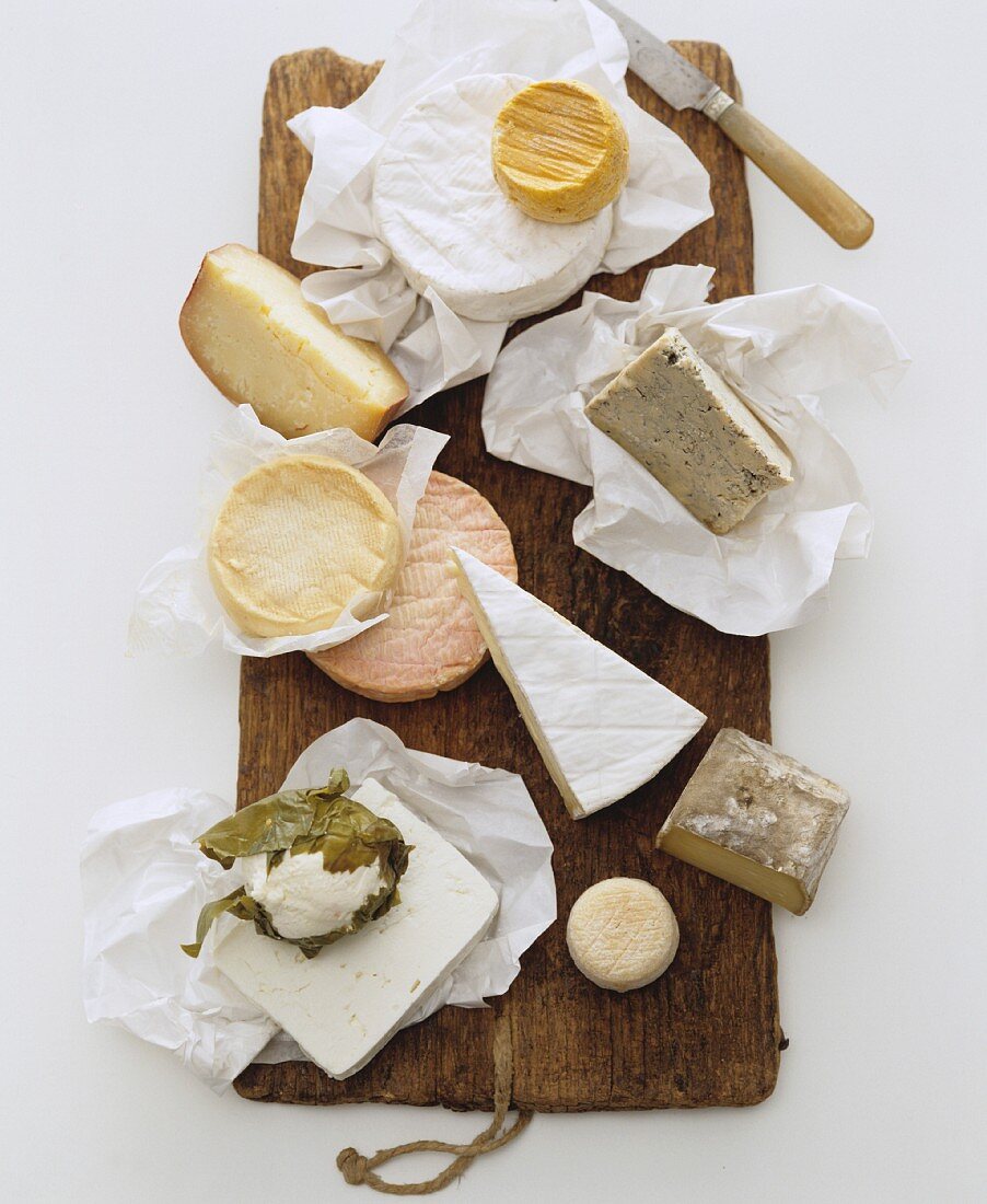 A still life featuring assorted cheeses on a wooden board (view from above)