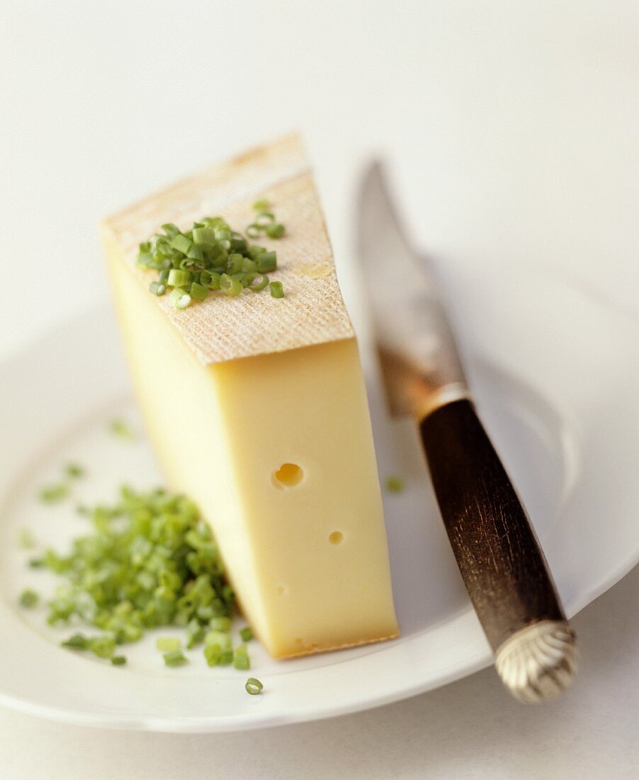 A slice of Raclette cheese on a plate with chives and a knife