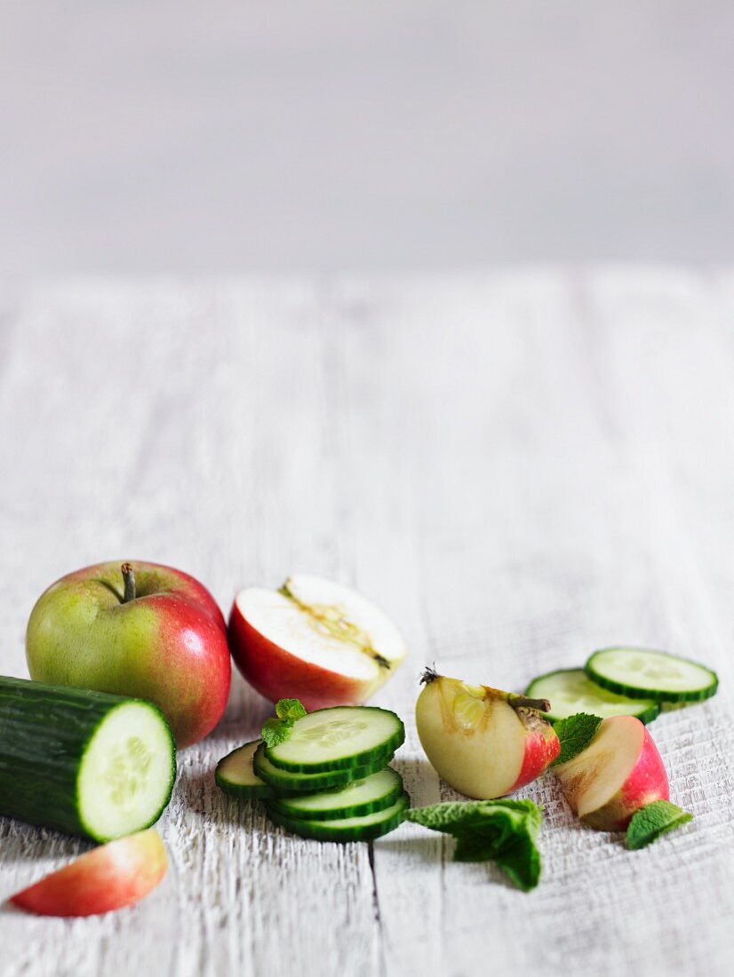 A still life featuring cucumber, apple and mint