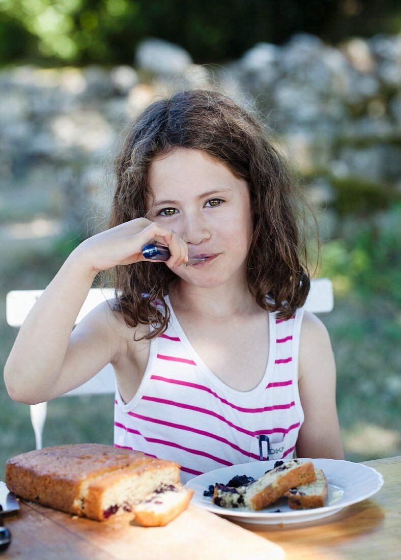 Mädchen isst Brombeerkuchen im Garten